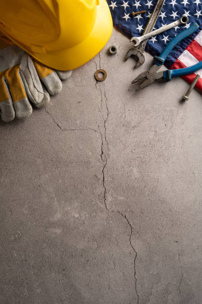 istock Yellow hard hat, gloves, tools, and American flag on cracked concrete vertical background symbolizing labor day in USA 2166615880