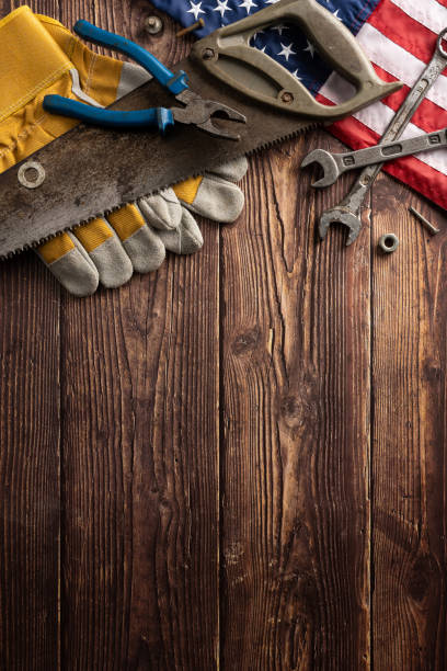 Various hand tools and work gloves with an American flag on a rustic vertical wooden background. Perfect for Labor Day themes