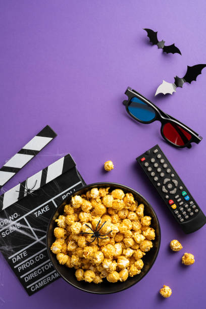 istock A bowl of popcorn with a spider and bats, 3D glasses, a remote, and a clapperboard on a vertical purple background 2166615896
