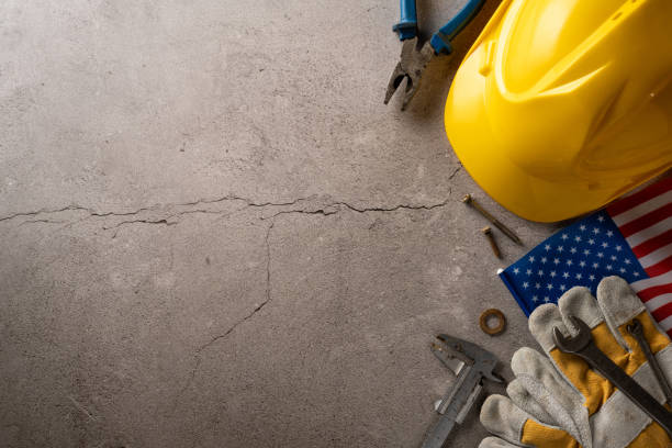 istock Yellow safety helmet and construction tools on a cracked concrete background with an American flag element 2166615899