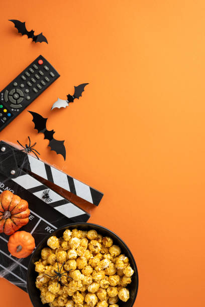 istock Festive Halloween setup featuring popcorn, remote control, clapboard, mini pumpkins, and bat decorations on an orange vertical background 2166615926
