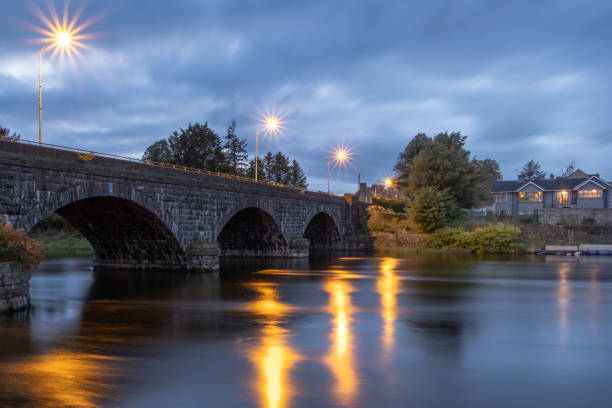 Porglenone, UK - October 8th, 2022: The bridge over the River Bann, golden starburst light from streetlights reflecting on water surface as dusk turns to night.