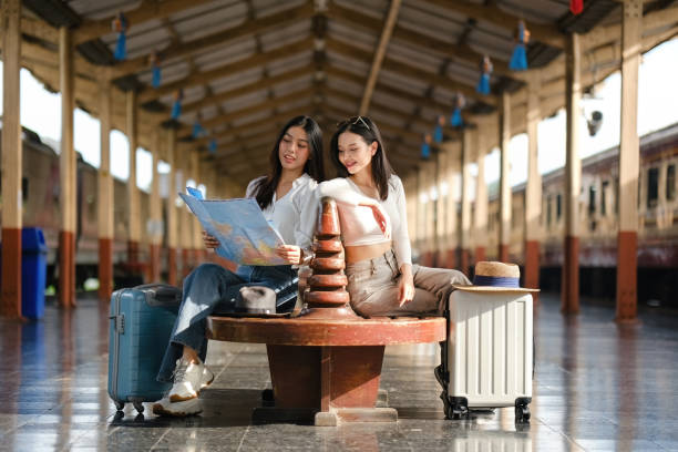 istock Two women sitting on a bench with suitcases and a map 2166633234