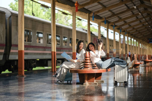 istock Two women sitting on a bench at a train station with suitcases 2166633269