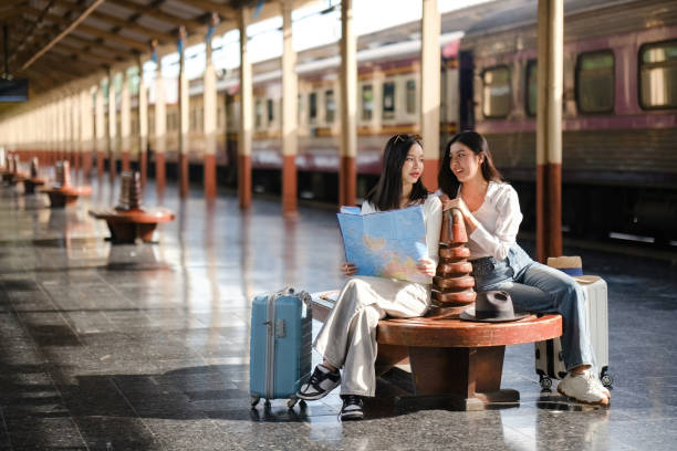 Two women sitting on a bench with suitcases and a map