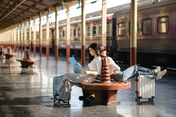istock Two women sitting on a bench at a train station with suitcases 2166633273