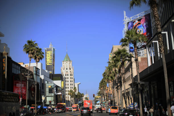 Hollywood boulevard, Los Angeles, California. Famous district, iconic place, walk of fame, theatre. Urban scene, stores, restaurants and shops, popular tourist attractions in America. Street view in summer time, big city. Blue sky and palm trees at sunset, tourists destination. Traffic, cars on the road,  shipping services. May 24, 2024. Top Travel Destination
