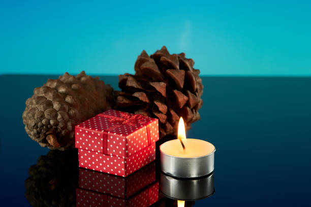 istock Holiday decor: pine cones, gift, and candle on shiny surface 2166641198