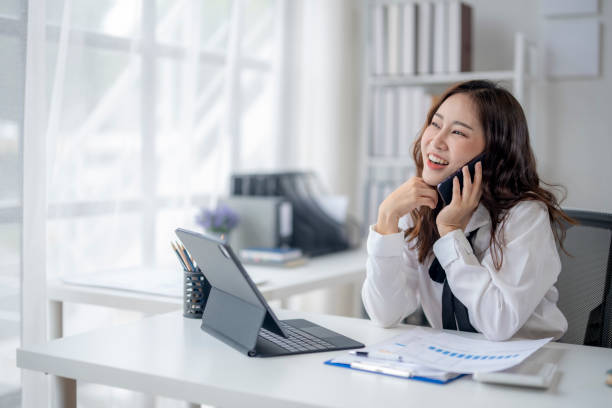 istock A woman is talking on her cell phone while sitting at a desk 2166643998
