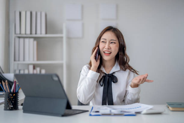 istock A woman is talking on her cell phone while sitting at a desk 2166645282