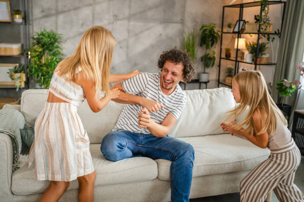 istock Daughters tickling their father on sofa at home have fun time together 2166658931