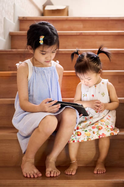 istock Sisters using digital tablet sitting together on stairs at home 2166667561