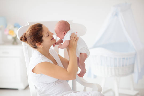 Young mother with newborn baby. Mom nursing little baby boy. Family at home. Infant care. Breastfeeding for kids health. White bedroom for little child.