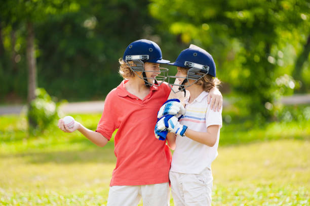 Kids playing cricket in summer park. Boy with bat and ball on cricket pitch. Helmet and guard for safe game. Sport for active child. Cricket club for school children. Sports activity and exercise.