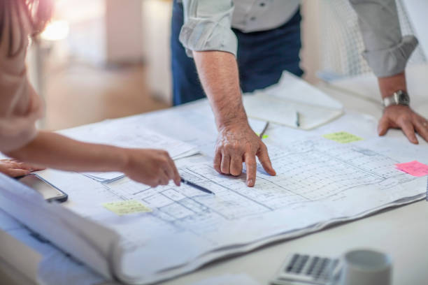istock Colleagues gesturing pointing at architectural plans on tabletop desk in office 2166668199