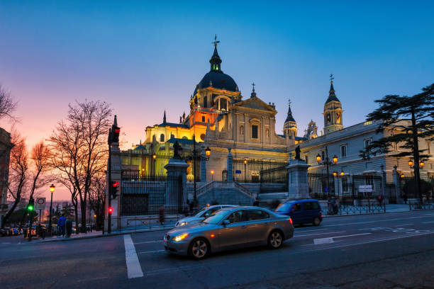 Cars stand at the landmark Almudena Cathedral (Santa Maria la Real de la Almudena) in downtown Madrid, Spain at twilight blue hour.