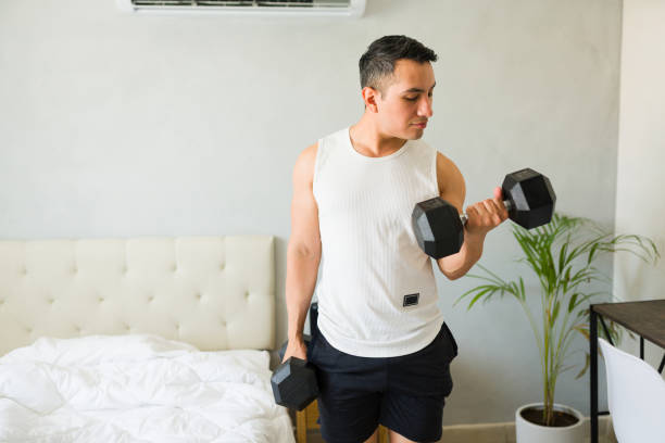 istock Focused young man lifting weights in bedroom, showing commitment to strength training and active lifestyle 2166686685