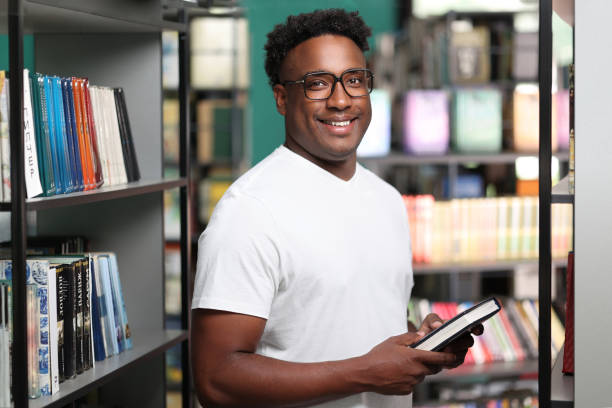 istock Young student in glass reading book while standing in modern university library 2166687116