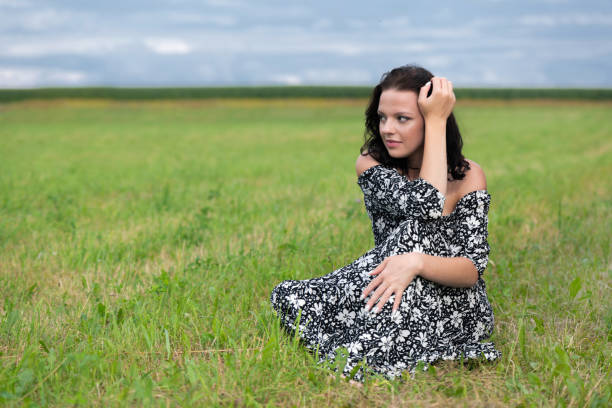 Blonde woman takes a quiet break, sitting on a field surrounded by nature, lost in thought and relaxation.