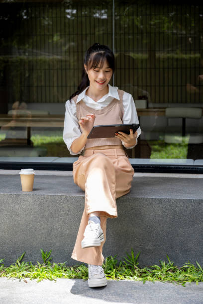 istock Asian woman in casual clothes is using her tablet while standing outdoors in a building area. 2166693342