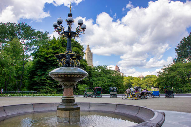 NYC, NY USA August 18, 2012: Where Victorian carriages once gathered, pedicabs wait for customers at the Cherry Hill Fountain in Central Park. San Remo Apartments is in the background.