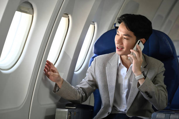istock Successful businessman in suit talking on mobile phone while sitting comfortable seat in airplane cabin. 2166698958