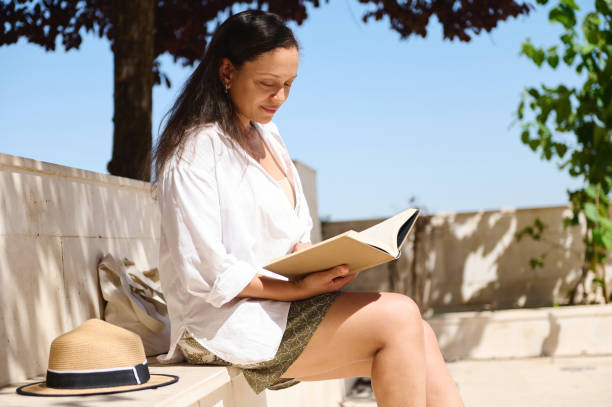 istock Woman reading a book outdoors on a sunny day in a park 2166703844