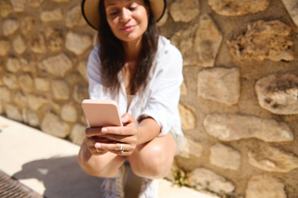 istock Young woman using smartphone outdoors by stone wall on a sunny day 2166703849