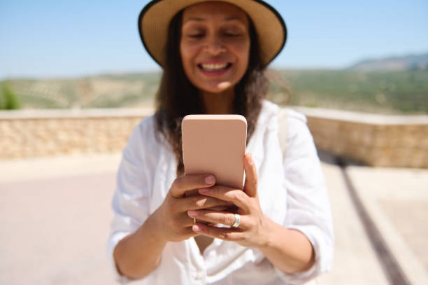istock Smiling woman using smartphone outdoors in a sunny day wearing a straw hat and white blouse 2166704112