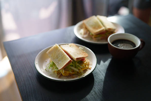 istock Homemade cabbage egg mayo sandwich served with a cup of black coffee on a table, with soft morning sunlight shining on it. 2166704411