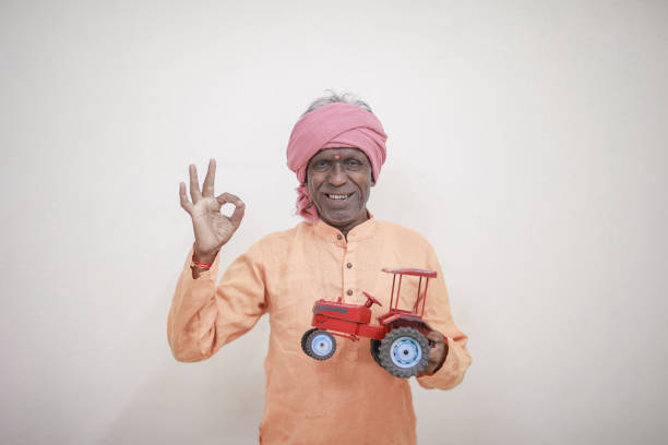 Indian farmer holding mini tractor toy for loan and banking , success of poor and old farmer