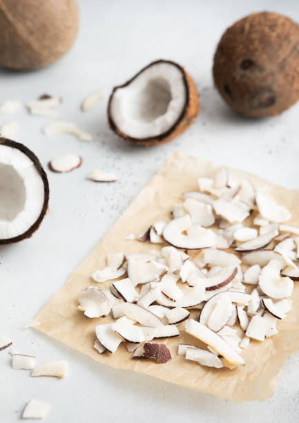istock Dried organic coconut slices chips on baking paper with whole ripe coconut on light background.Macro. 2166718682