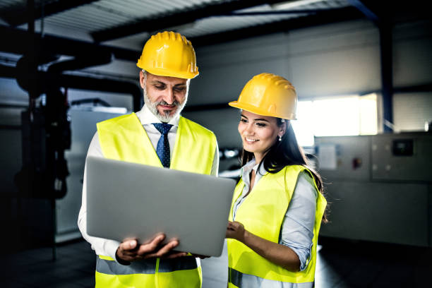 istock Two project managers standing in modern industrial factory, looking at laptop screen. Manufacturing facility with robotics, robotic arms and automation. Storing products and materials in warehouse. 2166718696