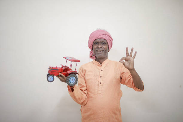 Indian farmer holding mini tractor toy for loan and banking , success of poor and old farmer