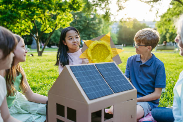istock Children learning about renewable energy and solar panels during sustainable education class outdoors, using cardboard model of house wit solar panel on roof. 2166719492