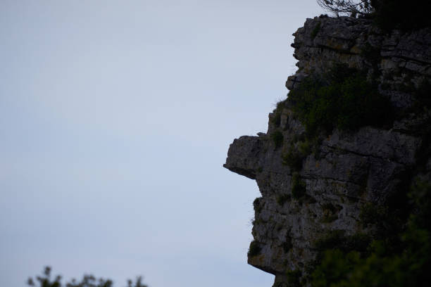 A captivating close-up of a rock formation, backlit to reveal its striking resemblance to human facial features. The silhouette highlights the natural contours and textures that evoke the essence of human form, offering a mesmerizing interplay between geology and imagination