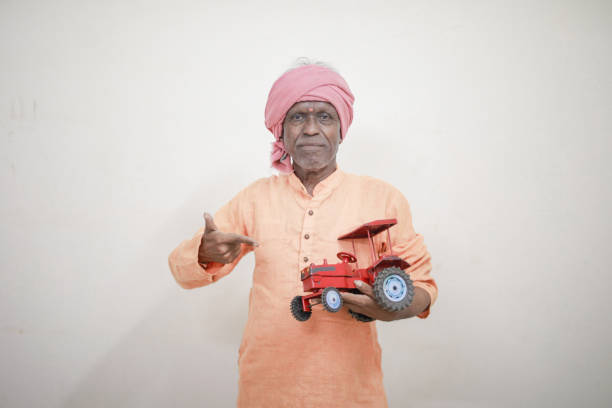 Indian farmer holding mini tractor toy for loan and banking , success of poor and old farmer
