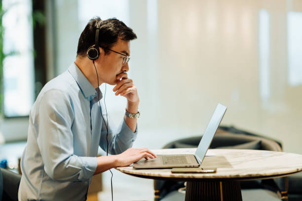 Asian businessman on videoconference with headset in modern office, capture the serious and contemplative emotions.