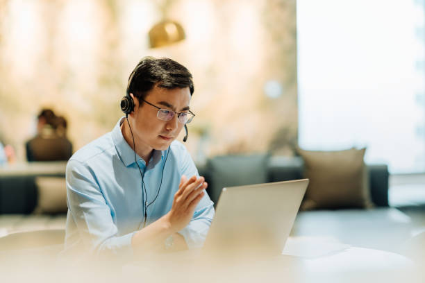 Asian businessman on videoconference with headset in modern office, capture the serious and contemplative emotions.