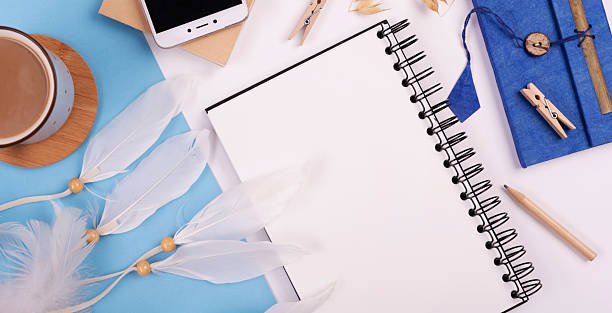 istock Office desk with empty spiral notebook, smart phone with device sreen and coffee cup. Office supply on blue background in boho styles. Place of work. Web banner. 2166735784