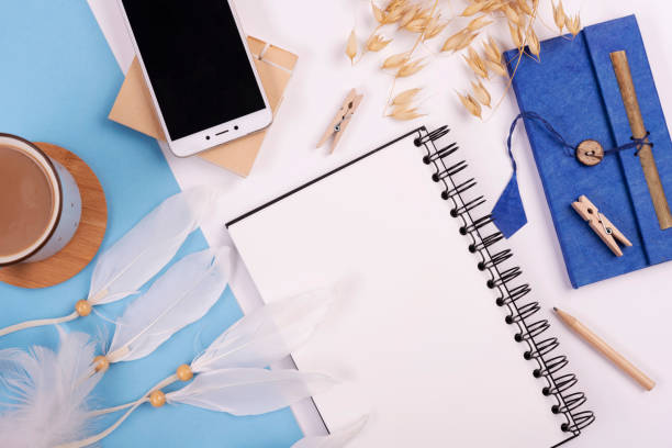 istock Office desk with empty spiral notebook, smart phone with device sreen and coffee cup. Office supply on blue background in boho styles. Place of work. Web banner. 2166735799
