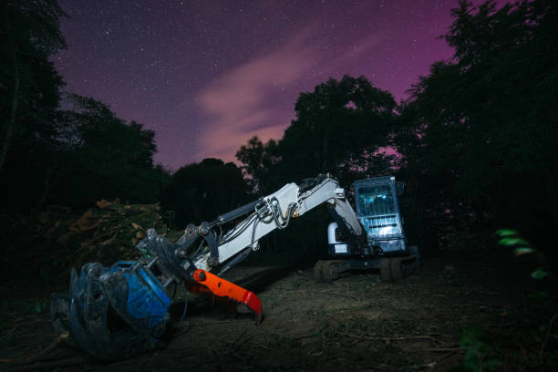 A compact excavator sits quietly in a dark forest after a day's work, with the Northern Lights, or Aurora Borealis, lighting up the sky in the background. Typically unseen this far south, the lights are visible tonight due to a powerful solar storm. Mullingar, Ireland, August 2024.