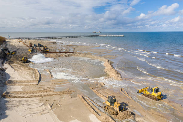 istock Beach restoration sand Bulldozers. Mud flows from the pipe with excavator behind for the reconstruction of the beach taken away by the sea. Work in progress for beach nourishment. Drone shot. 2166738584