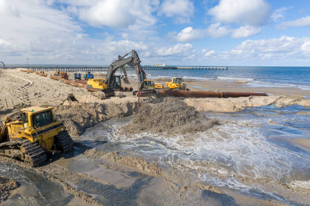 istock Beach restoration sand Bulldozers. Mud flows from the pipe with excavator behind for the reconstruction of the beach taken away by the sea. Work in progress for beach nourishment. Drone shot. 2166738598
