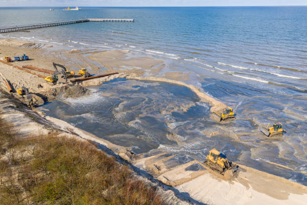 istock Beach restoration sand Bulldozers. Mud flows from the pipe with excavator behind for the reconstruction of the beach taken away by the sea. Work in progress for beach nourishment. Drone shot. 2166738842