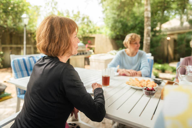 Side view of a Caucasian woman and her adult daughter talking at a table during a family meal in the garden, her grandson sitting at the table in the background