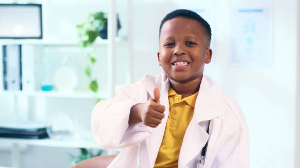 istock Smiling Young Boy Dressed as a Doctor Giving a Thumbs Up in a Bright Modern Clinic Setting 2166739669