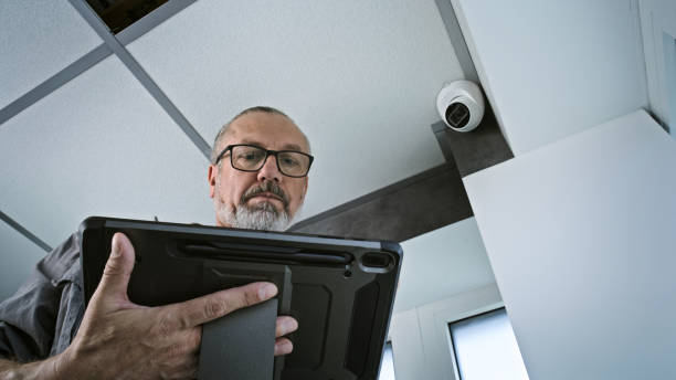 istock Male installer adjusts the angle of CCTV camera in office, uses tablet computer 2166740229