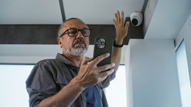 istock Male mature technician sets up CCTV camera in office building using mobile phone 2166740411