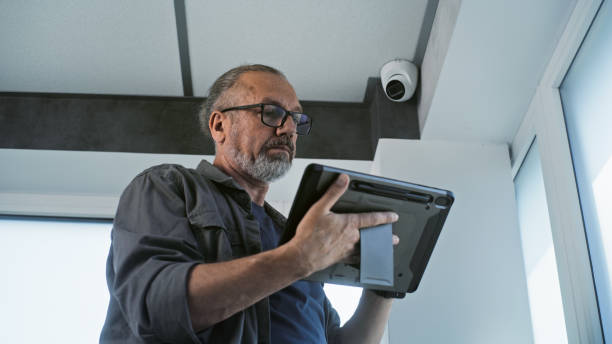 istock Male mature installer sets up CCTV camera in office room using tablet computer 2166740700